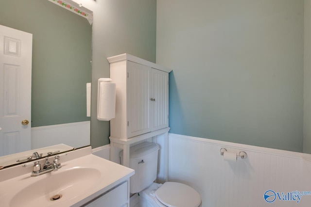 bathroom with toilet, vanity, and wainscoting