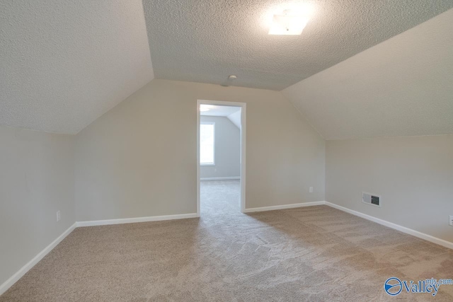 additional living space featuring a textured ceiling, baseboards, lofted ceiling, carpet flooring, and visible vents