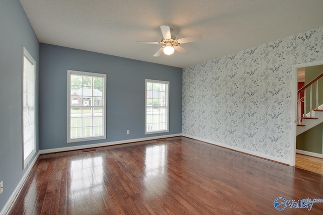 spare room with stairway, wood finished floors, wallpapered walls, ceiling fan, and baseboards