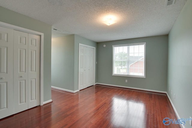 unfurnished bedroom with wood finished floors, a textured ceiling, multiple closets, baseboards, and visible vents