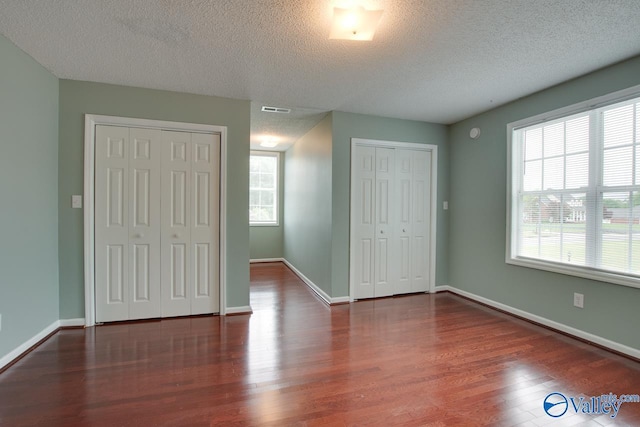 unfurnished bedroom featuring visible vents, multiple closets, wood finished floors, and multiple windows