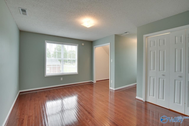 unfurnished bedroom with a textured ceiling, hardwood / wood-style floors, visible vents, and a closet