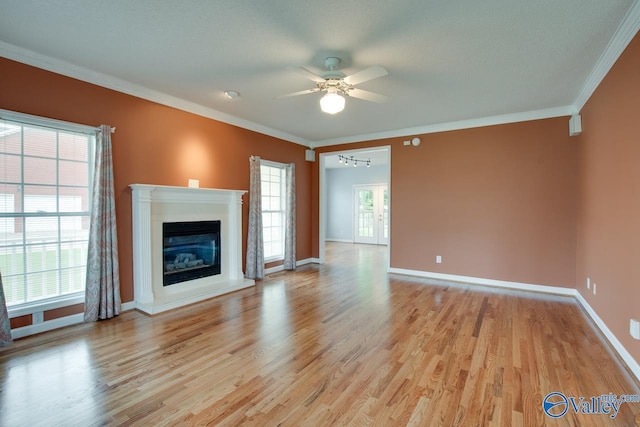 unfurnished living room with light wood-type flooring, a glass covered fireplace, ceiling fan, and crown molding