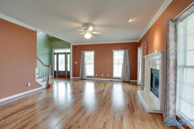 unfurnished living room with stairway, a ceiling fan, light wood-style floors, crown molding, and a fireplace