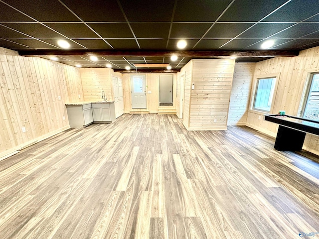 basement with a paneled ceiling, light hardwood / wood-style flooring, wood walls, and sink