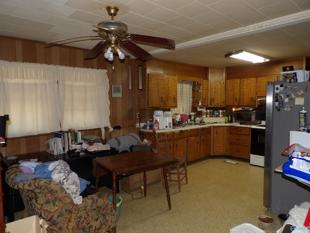 kitchen with ceiling fan, wooden walls, stainless steel fridge, and white electric stove