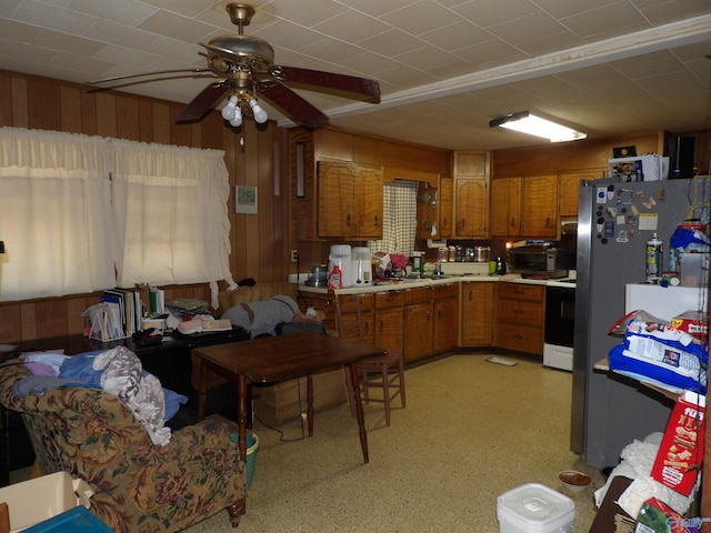 kitchen with wood walls, ceiling fan, white range, and stainless steel refrigerator