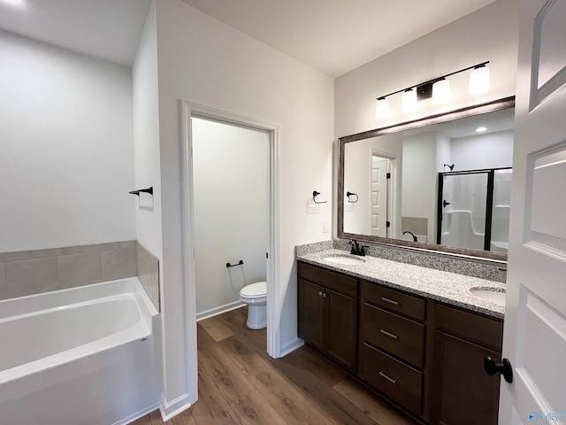 bathroom featuring toilet, wood finished floors, a sink, double vanity, and a stall shower