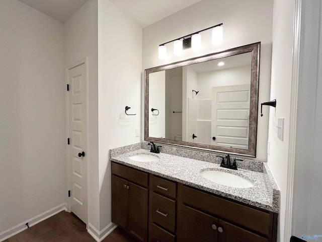 bathroom featuring walk in shower, a sink, baseboards, and double vanity