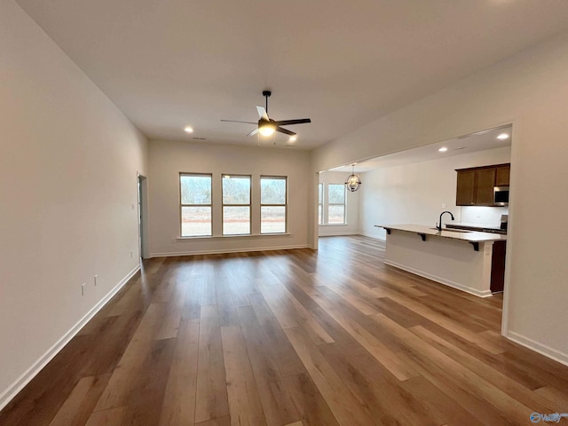 unfurnished living room featuring recessed lighting, dark wood finished floors, baseboards, and ceiling fan with notable chandelier