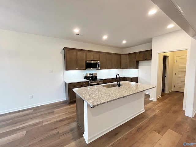 kitchen with stainless steel appliances, wood finished floors, an island with sink, and a sink