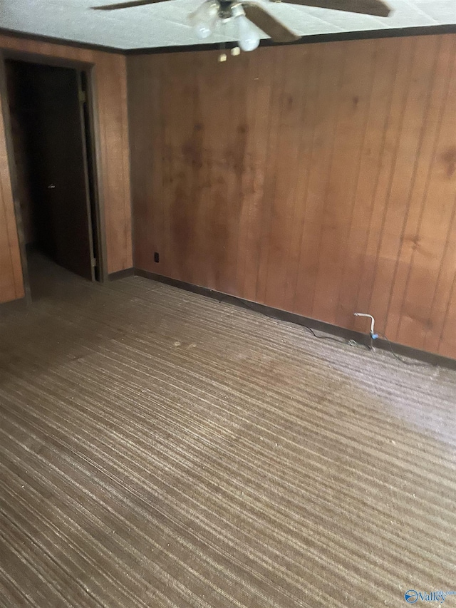 empty room featuring ceiling fan and wood walls