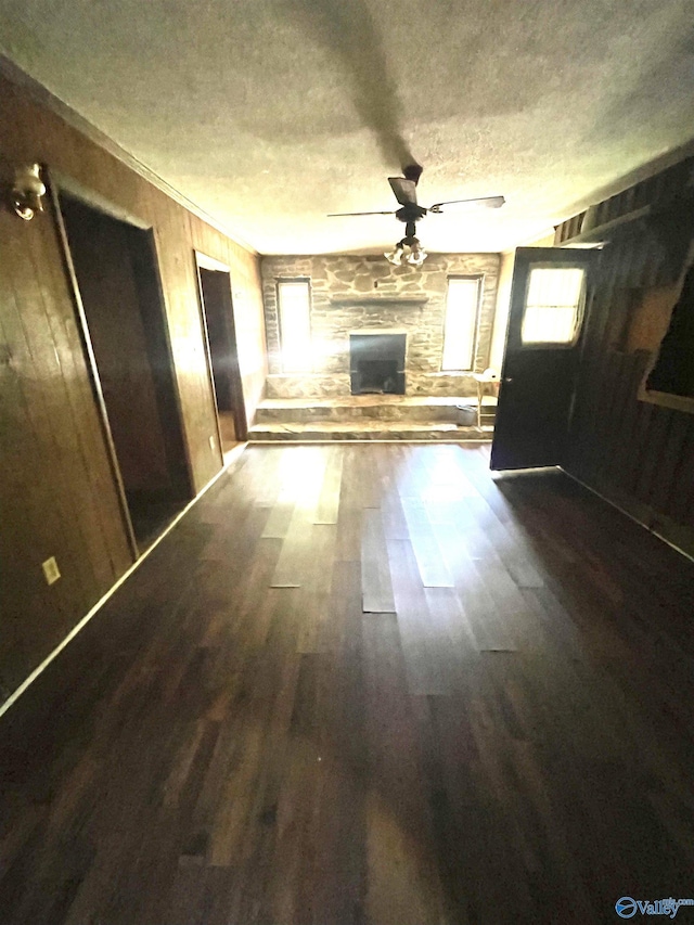 unfurnished living room with wood walls, ceiling fan, dark wood-type flooring, and a textured ceiling