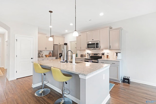 kitchen featuring hardwood / wood-style flooring, sink, an island with sink, hanging light fixtures, and appliances with stainless steel finishes