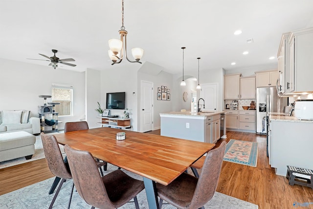 dining space with ceiling fan with notable chandelier, light wood-type flooring, and sink