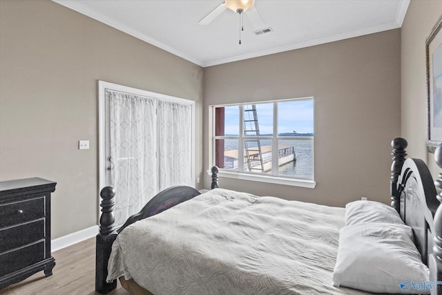 bedroom featuring visible vents, wood finished floors, baseboards, a water view, and ornamental molding