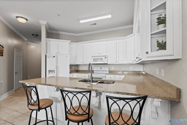 kitchen featuring a peninsula, white appliances, a breakfast bar area, white cabinets, and a sink