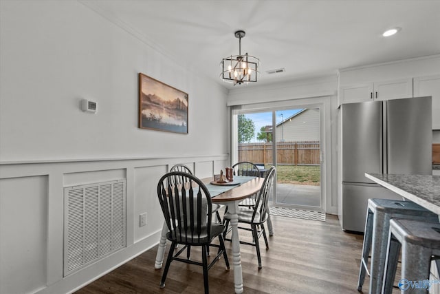 dining space with ornamental molding, visible vents, an inviting chandelier, and wood finished floors