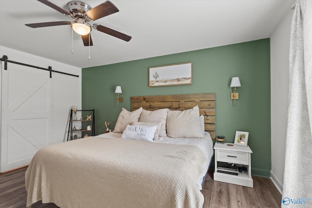 bedroom with baseboards, a barn door, ceiling fan, and wood finished floors