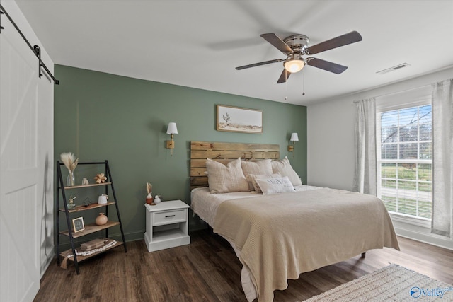 bedroom featuring visible vents, baseboards, wood finished floors, a ceiling fan, and a barn door