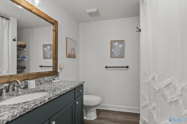 bathroom with vanity, toilet, baseboards, visible vents, and wood finished floors