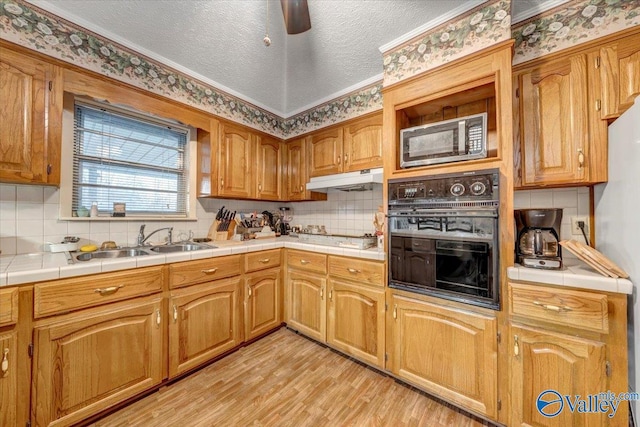 kitchen with black oven, light hardwood / wood-style flooring, sink, tasteful backsplash, and tile counters