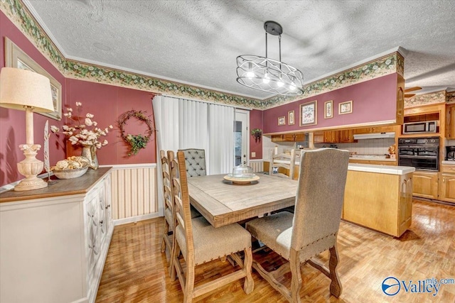 dining space featuring a textured ceiling, ornamental molding, and light wood-type flooring