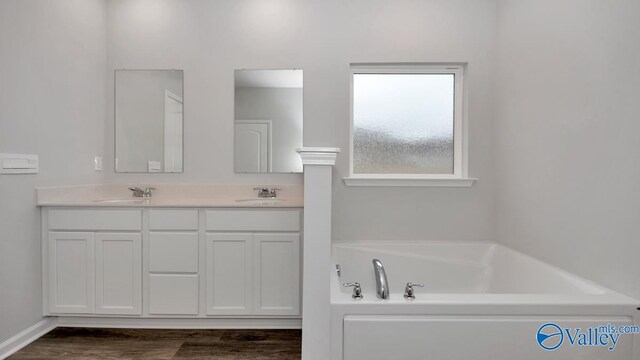 full bath with double vanity, a sink, a garden tub, and wood finished floors