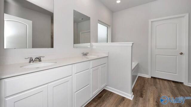 bathroom with a bath, double vanity, a sink, and wood finished floors