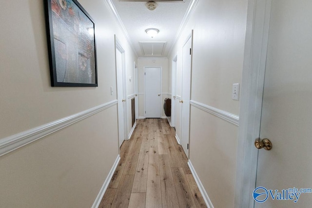 hall featuring light wood-type flooring, attic access, baseboards, and crown molding