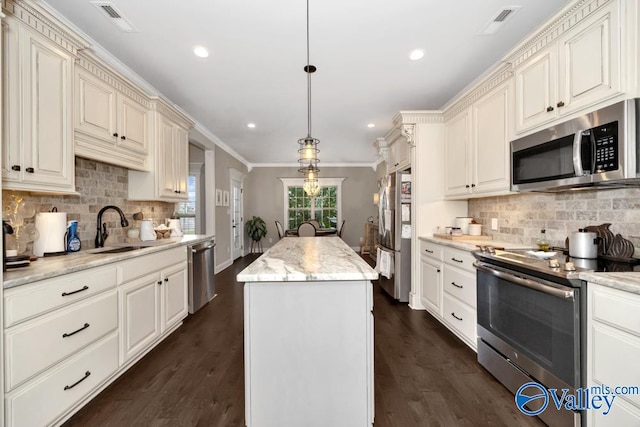 kitchen with light stone countertops, sink, a center island, decorative light fixtures, and appliances with stainless steel finishes