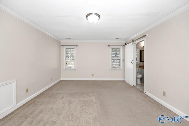 carpeted spare room with a barn door, baseboards, and crown molding