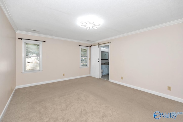 carpeted spare room featuring a barn door, visible vents, and crown molding