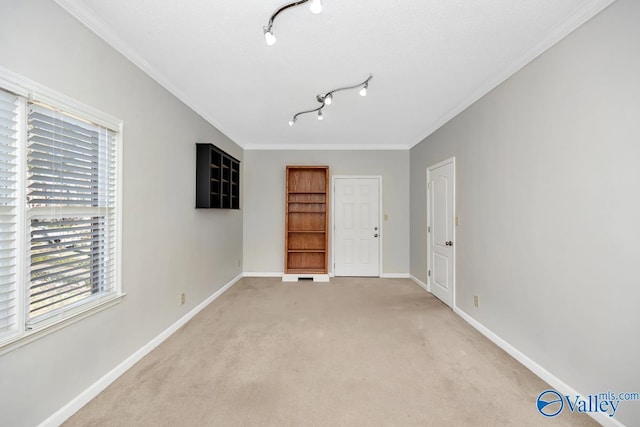 spare room with rail lighting, ornamental molding, baseboards, and light carpet