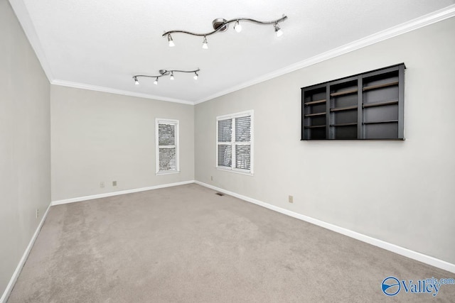 spare room with carpet flooring, track lighting, baseboards, and ornamental molding