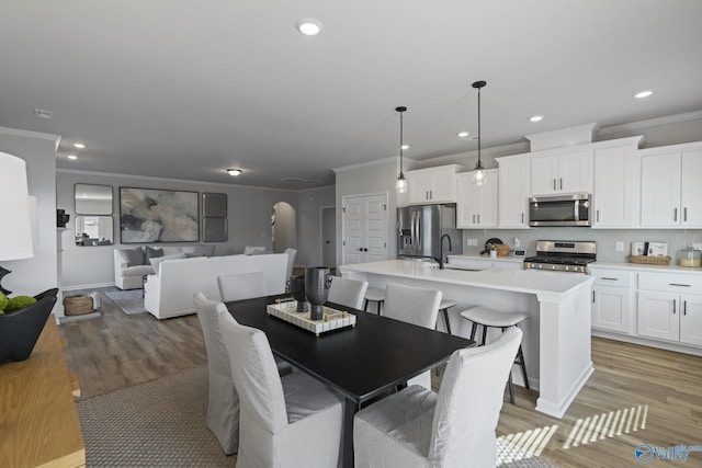 dining area with ornamental molding, arched walkways, light wood-style flooring, and recessed lighting