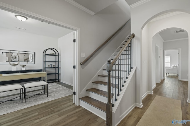 stairway with crown molding, baseboards, arched walkways, and wood finished floors