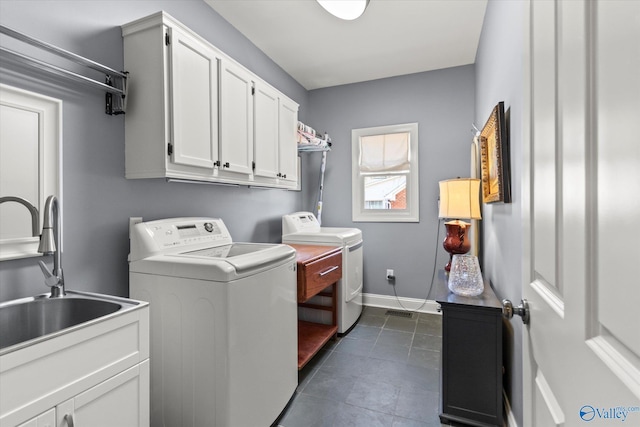 laundry area featuring dark tile patterned floors, washer and dryer, a sink, cabinet space, and baseboards