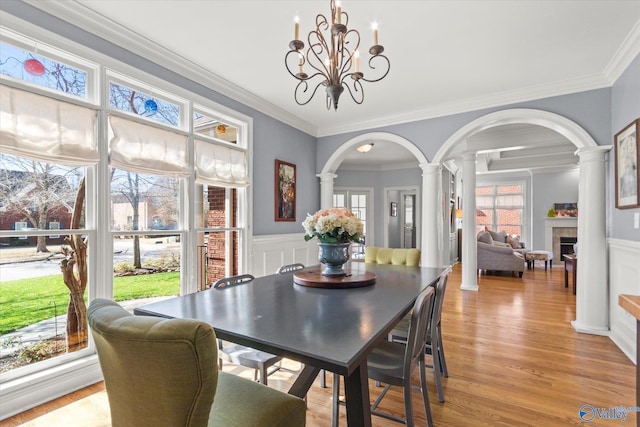 dining room featuring light wood finished floors, arched walkways, wainscoting, and ornate columns