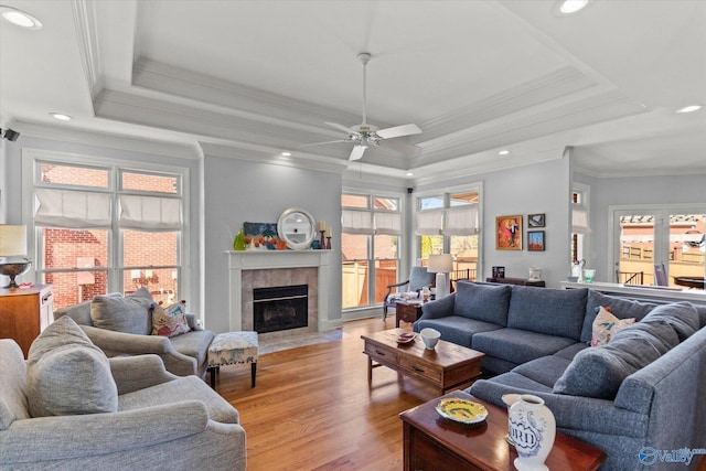 living room with recessed lighting, a tray ceiling, light wood-style flooring, and a tiled fireplace