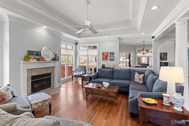 living room with crown molding, a tray ceiling, ceiling fan with notable chandelier, a fireplace, and wood finished floors