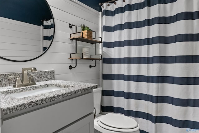 bathroom with vanity, wooden walls, toilet, and a shower with curtain