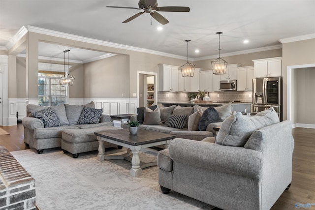 living room with a wainscoted wall, ornamental molding, recessed lighting, ceiling fan with notable chandelier, and wood finished floors