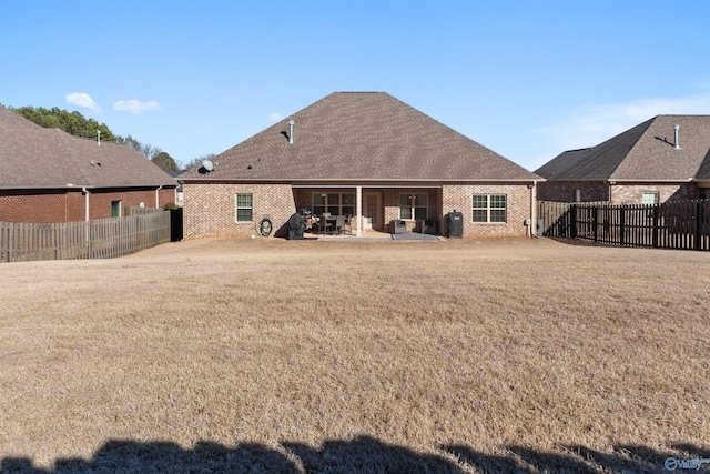 rear view of property featuring a yard, a patio, brick siding, and a fenced backyard