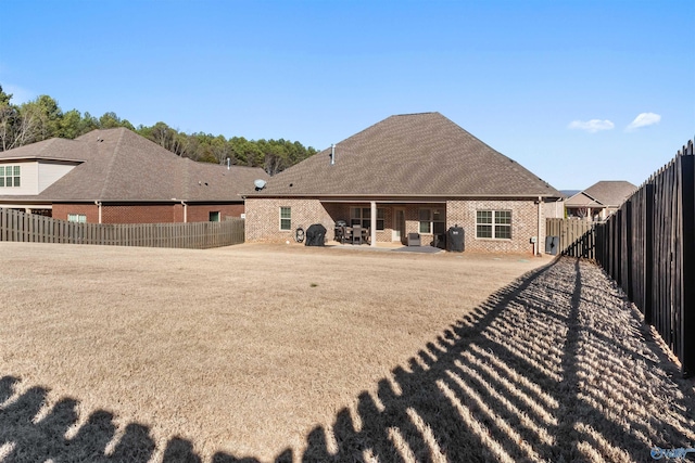 rear view of property with a patio area, brick siding, a fenced backyard, and roof with shingles