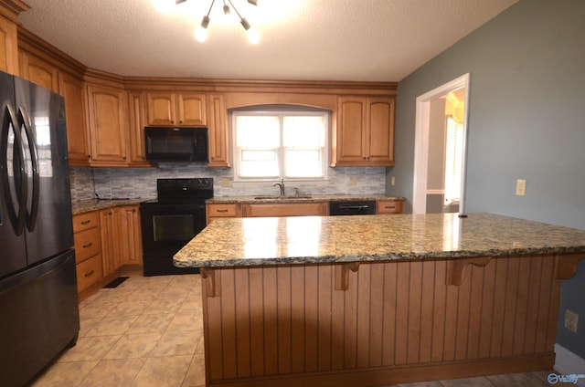 kitchen with light stone counters, sink, black appliances, and a breakfast bar