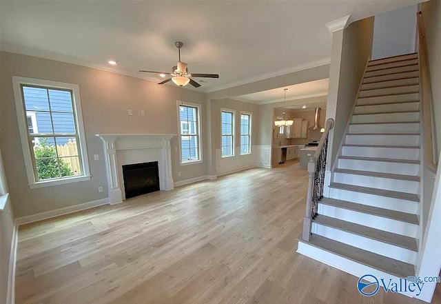 unfurnished living room with crown molding, a healthy amount of sunlight, ceiling fan with notable chandelier, and light wood-type flooring