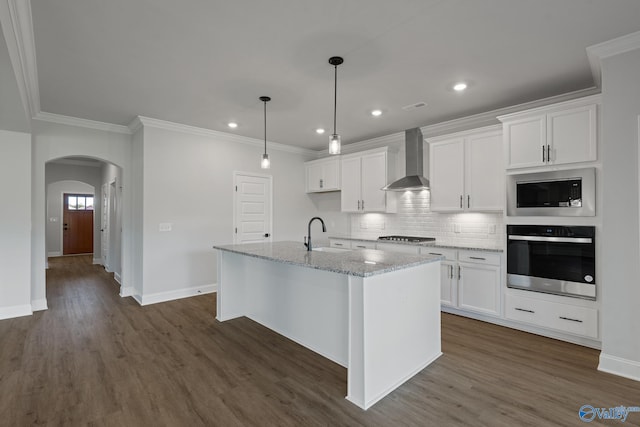 kitchen featuring appliances with stainless steel finishes, dark hardwood / wood-style flooring, wall chimney exhaust hood, a kitchen island with sink, and white cabinetry