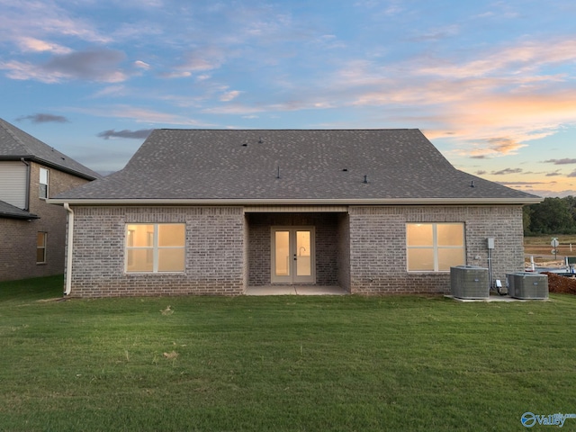 back house at dusk with a yard, a patio, and central AC