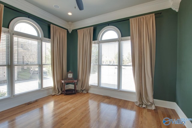 empty room with plenty of natural light, wood finished floors, visible vents, and baseboards